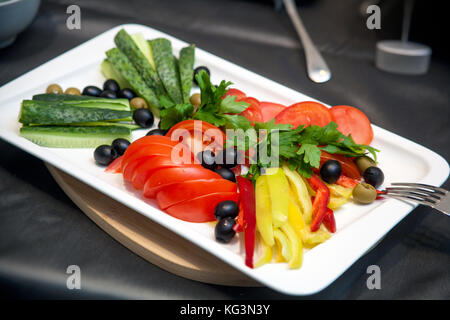 Gros plan sur une plaque blanche est coupé en tranches de légumes frais : concombres, poivrons, tomates, olives, les verts Banque D'Images