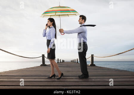 Businessman holding umbrella pour femme sur boardwalk over sea Banque D'Images