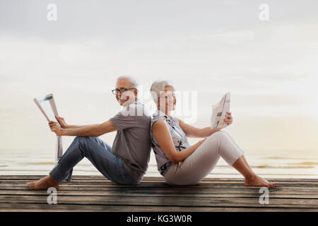 Senior couple sitting on wooden dock près du lac et reading newspaper Banque D'Images