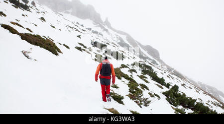 Un homme marche seul sur une randonnée en montagne. Le temps semble si froid et le vent est fort mais il doit continuer à traverser la neige. Banque D'Images