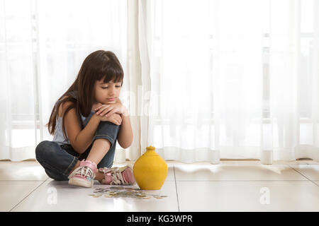 Petite fille assise sur le plancher avec de l'argile tirelire et pièces Banque D'Images