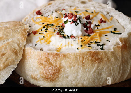 Soupe de pommes de terre chaude avec de la crème sure, le fromage cheddar, bacon et la ciboulette, dans un bol de pain au levain frais. L'extrême profondeur de champ avec Banque D'Images