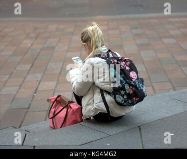 Jeune fille coloré student sitting on steps avec le smartphone et un sac à dos vu de derrière Banque D'Images