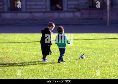 Les jeunes enfants kids les petits garçons une noire une blanche à la poursuite d'un pigeon sur l'herbe vu de derrière Banque D'Images