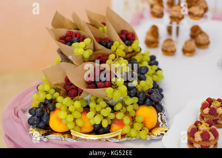 Les desserts sucrés avec des baies et des fruits servis sur la table.buffet servi raisins fruits,framboises,les pêches dans des sacs en papier. Banque D'Images