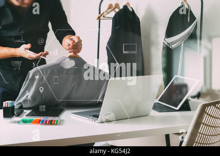 Fashion designer holding shirt and using laptop with digital tablet computer in studio moderne avec schéma de l'icône de VR Banque D'Images