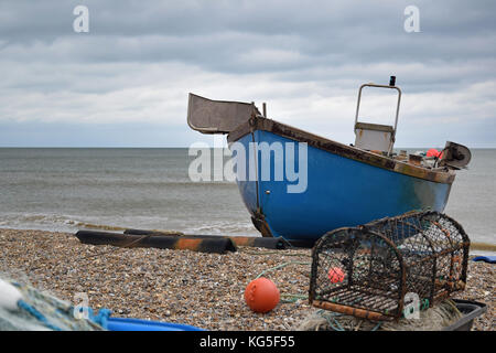 Bateau de pêche bleu sur une plage de galets à Aldeburgh, dans le Suffolk avec un lobster pot en face Banque D'Images