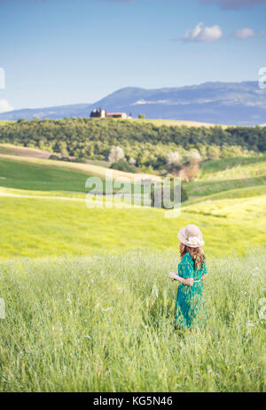 Une fille dans une robe verte marchant dans les champs dorés de la Toscane. Val d'Orcia, province de Sienne, Toscane, Italie Banque D'Images