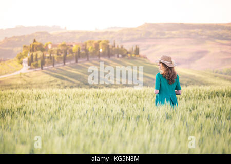 Une fille dans une robe verte marchant dans les champs dorés de la Toscane. Val d'Orcia, province de Sienne, Toscane, Italie Banque D'Images