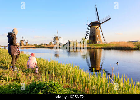 La mère et l'enfant d'admirer les moulins à vent typiques reflétée dans le molenwaard kinderlijk canal South Holland aux Pays-Bas l'Europe Banque D'Images