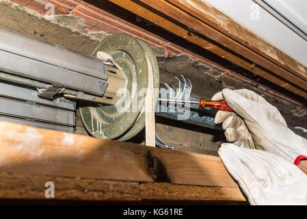 Réparation de volet roulant. Ajuste un travailleur de volets roulants cassés d'une maison. Close-up des mains avec des gants et des tournevis démarreur orange Banque D'Images
