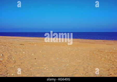 Un désert de sable avec la mer bleue au-delà vu sous un ciel bleu clair. Banque D'Images