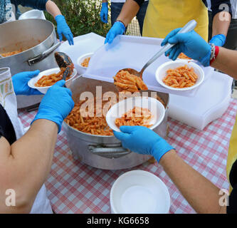 Les mains avec des gants en latex bleu lors de la distribution de repas avec des pâtes et de la sauce tomate à la cantine Banque D'Images