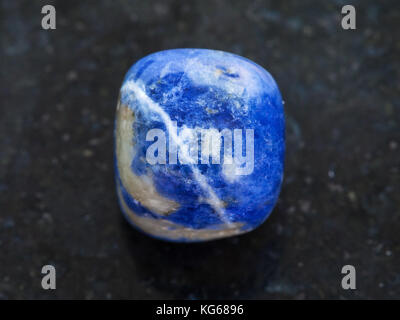 La prise de vue macro des eaux minérales naturelles rock specimen - tumbled gemstone sodalite sur fond de granit sombre Banque D'Images