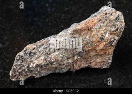 La prise de vue macro des eaux minérales naturelles rock specimen - brut de la syénite à néphéline biotite pierre sur l'arrière-plan en granit sombre Banque D'Images