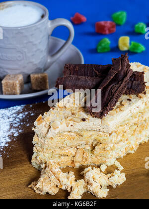 Morceau de gâteau sablé aux noix, en miettes et décoré de chocolat sur une planche à découper en bois sur une nappe bleue avec une tasse de café et candie Banque D'Images