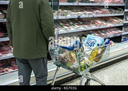 Un homme avec un panier plein d'épicerie dans un supermarché Tesco allée de la viande fraîche. L'Écosse, Royaume-Uni Banque D'Images