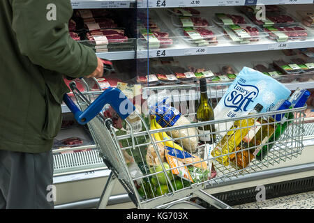 Un homme avec un panier plein d'épicerie dans un supermarché Tesco, le choix de la viande, Ecosse, Royaume-Uni Banque D'Images