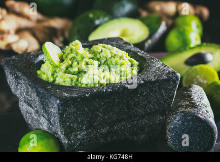 Sauce guacamole mexicain latino-américains avec de l'avocat, du gingembre et de la chaux dans le mortier en pierre et ingrédients - avocat frais palta, gingembre, citron vert sur noir backg Banque D'Images