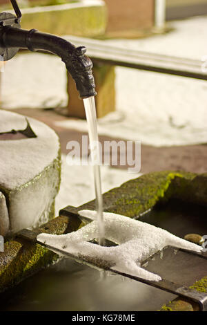 Une petite fontaine en hiver la nuit avec de la glace et de la neige. Banque D'Images