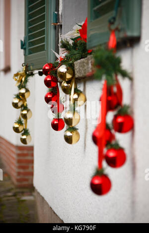 Le rouge et or boules de noël suspendu à une fenêtre sur une maison. Banque D'Images