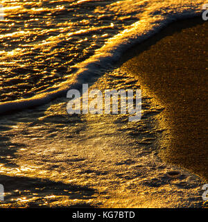 Close-up of abstract colorful formes créées par les vagues sur une plage de sable et de réflexions soleil au coucher du soleil Banque D'Images