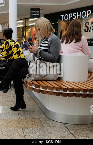 2017 octobre - une jeune femme se reposant à regarder son smartphone sur une place au milieu du centre commercial Cribbs Causeway à Bristol, dans le sud-ouest. Banque D'Images