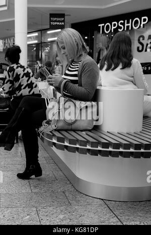 2017 octobre - une jeune femme se reposant à regarder son smartphone sur une place au milieu du centre commercial Cribbs Causeway à Bristol, dans le sud-ouest. Banque D'Images