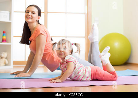 Mère et enfant fille faisant les exercices de yoga sur le plancher dans la pièce à la maison. de l'intérieur, avec la remise en forme. Banque D'Images