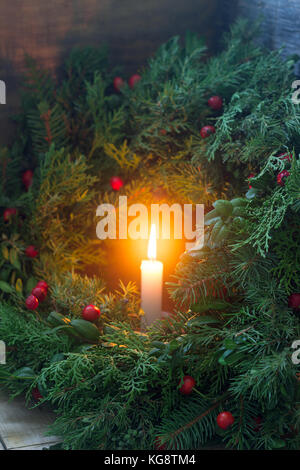 Une couronne de Noël faite de branches de sapin, genévrier, tuja, buis et Wild Rose baies. couronne, avec des bougies allumées. Banque D'Images