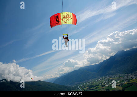 Parachutiste est volant sous son parachute et d'aller à terre sur l'herbe verte. Il est ainsi le ralentissement de l'auvent en tirant les pauses. Banque D'Images