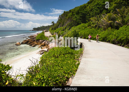 Les Seychelles, La Digue, Anse Formis, deux touristes âgés à vélo sur la route de la côte est vide Banque D'Images