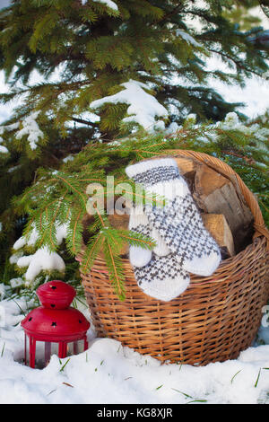 Mitaines en laine sur le bois de basketful près de snowy christmas-tree et une lanterne rouge de style scandinave. Banque D'Images