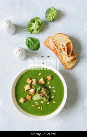 Soupe crème de brocoli avec les croûtons et les pignons de pin dans un bol blanc. table top view, vertical Banque D'Images