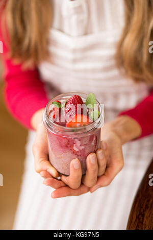 La fille de cuisine est titulaire d'un pot de dessert de fruits et les fraises dans ses mains Banque D'Images