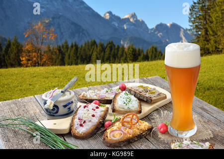 Petit snack avec différents types de pâtes à tartiner sur pain de campagne servi avec une bière de blé levure fraîche sur une vieille table en bois dans les Alpes bavaroises Banque D'Images