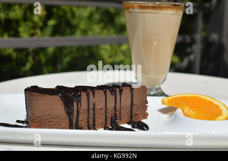 Gâteau au chocolat avec garniture riche et une tranche d'orange - sur la plaque en porcelaine blanche - et un verre de café à la crème ou un macchiato Banque D'Images