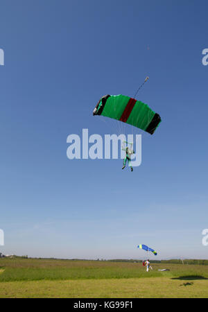 Ce parachutiste est volant sous sa verrière dans le ciel. Bientôt il va atterrir son parachute vert et noir sur l'herbe. Banque D'Images