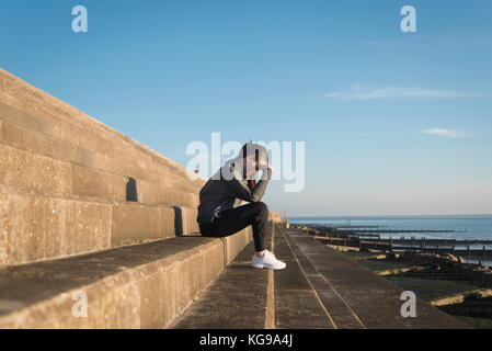 Femme assise sur des mesures en dehors de la mer avec sa tête dans ses mains Banque D'Images