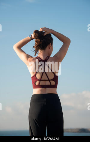 Femme sportive attachant ses cheveux en place avant de commencer l'exercice et de formation portant un soutien-gorge de sport, vue de dos. Banque D'Images