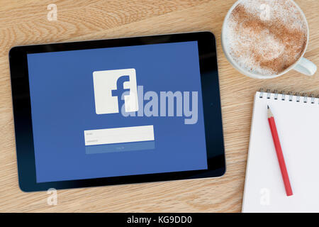 Le site Facebook fonctionnalités sur un iPad tablet device qui repose sur une table en bois à côté d'un bloc-notes et un crayon et une tasse de café (rédaction uniquement) Banque D'Images