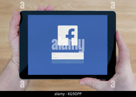 Un homme regarde le site Facebook sur son iPad tablet device, tourné contre une table en bois page contexte (usage éditorial uniquement) Banque D'Images