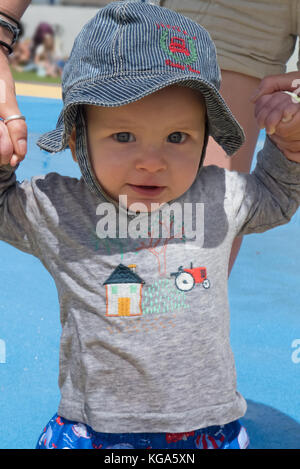 Huit mois bébé garçon dans une disquette sun-hat, se tenant la main et de l'aide pour marcher. Parution du modèle Banque D'Images