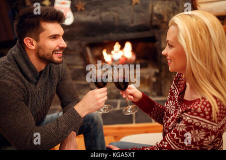 Femme souriante et man toasting délicieux vin rouge à cheminée romantique Banque D'Images