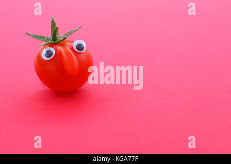 Tomate cerise mûre fraîche avec un visage sur un fond uni avec copie espace Banque D'Images