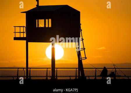 Un pêcheur regarde le soleil se lève sur la baie de Cardiff, Cardiff, Pays de Galles en barrage. Les prévisionnistes ont prédit une semaine de froid qui a été proposée à Banque D'Images
