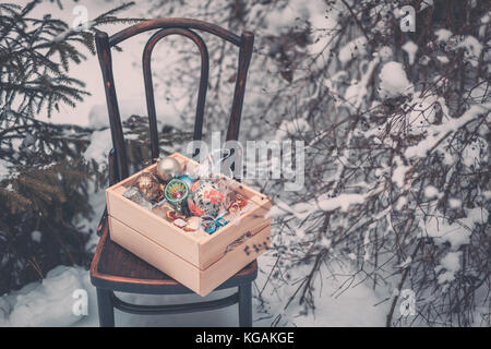 Boules de décoration de Noël dans une boîte en bois à l'extérieur, sur fond de neige en hiver Banque D'Images