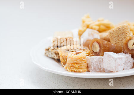 Variété de douceurs orientales au miel dans une assiette blanche sur un fond clair, les sucreries turques concept. Banque D'Images