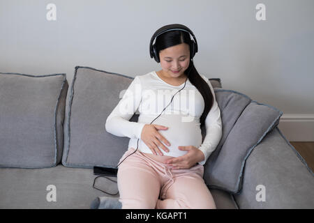 Femme enceinte à l'écoute de la musique sur le casque à la maison Banque D'Images