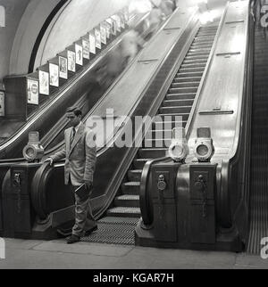 Début 1950s, photo historique montrant un homme bien habillé à l'étranger visiteur en Angleterre laissant le bas escalier roulant dans son voyage sur le métro de Londres, Londres, Angleterre, Royaume-Uni. Banque D'Images